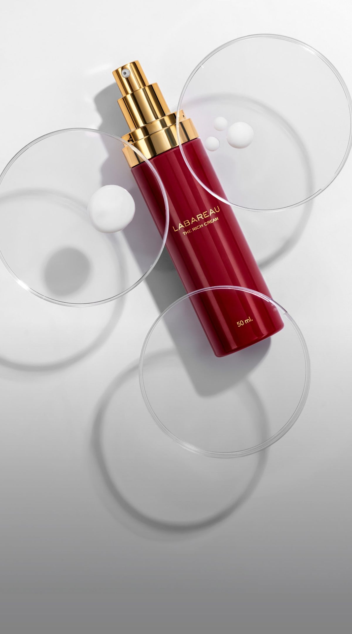 The Rich Cream 50 ml, rode airless flacon met gouden dop, op glazen petrischaaltjes